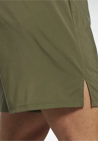 Olivově zelené sportovní šortky s hladkou texturou, se stranovými rozparky a šitými lemy pro lepší pohyblivost. Minimaalistický design, bez vzorů.