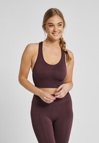 Bordeauxrode sportbeha met een ronde halslijn, brede bandjes en een nauwsluitend ontwerp. De stof heeft een geribbelde textuur voor extra ondersteuning.