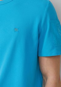 Korte mouwen, turquoise poloshirt met een gestructureerde stof en een klein logo op de linkerkant van de borst. Heeft een eenvoudig ontwerp met een ronde hals.