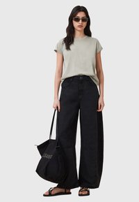 T-shirt verde chiaro a girocollo, jeans neri a gamba larga, sandali neri con dettagli dorati e borsa tote nera con logo.