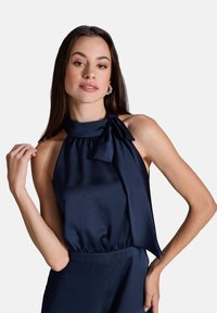 Haut dos nu marine en satin avec un détail de nœud noué au cou, présentant une taille élastiquée et une texture lisse.
