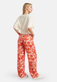Hellbeige Oberteil mit kurzem Arm und entspannter Passform, kombiniert mit hochtaillierten, lockeren Hosen mit einem lebhaften Blumenmuster in Orange und Pink.
