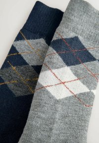 Stricksocken mit einem gemischten Design aus Marineblau und Grau, mit geometrischen Argyle-Mustern in Weiß, Orange und Gelb. 