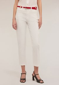 Witte cropped broeken met een slim fit, gecombineerd met een rode leren riem met gouden hardware. Zwarte haksandalen met een slangenprint.
