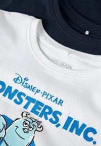 T-shirts blancs et bleu marine avec le logo Disney Pixar Monsters, Inc. et le personnage Sulley visible sur le t-shirt blanc.