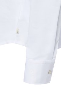 Weißes Hemd mit glatter Textur, ausgestattet mit einem Knopfmanschette und gesticktem Logo-Detail. Beinhaltet ein Etikett in der Nähe der Seitennaht für Branding.