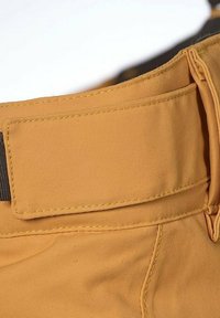 Beige kangasvyö, jossa on teksturoitu pinta, tummempi koristeteippi ja näkyvät saumat. Sopii housuille tai shortseille.