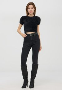 Top corto nero e morbido con maniche corte, abbinato a jeans neri con decorazioni di perline e stivali neri con tacco alti fino al ginocchio.