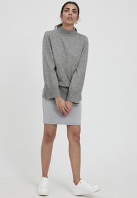 Top gri, cu mâneci lungi, gât înalt și croi ușor supradimensionat. Combinate cu o fustă gri ajustată și adidași albi. Design simplu, textură moale.