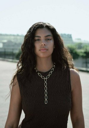 Haut sans manches texturé marron avec un long collier en or composé de maillons ovales et d'un pendentif unique suspendu à l'avant.