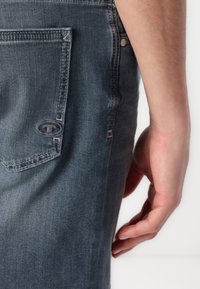 Denim jeans med en falmet grå farve, fem-lomme design og forstærkede syninger. Bemærkelsesværdigt logo på baglommen.