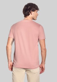 Světle růžové tričko s krátkým rukávem vyrobené z jemné bavlny. Má klasický kulatý výstřih a volný střih. Jemná struktura s čistými lemy.