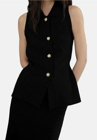 Haut noir sans manches avec col, boutons dorés, design structuré et silhouette évasée, réalisé en tissu texturé.