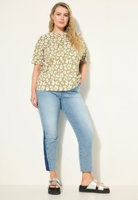 Zelený top s květinovým potiskem a krátkými rukávy, spárovaný s světle modrými džíny s námořnickým bočním pruhem, a stříbrnými sandály s tlustou podrážkou.