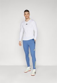 White long-sleeve shirt with black logo, blue athletic pants with yellow accents and stripes, and white sports shoes. Minimalist design.