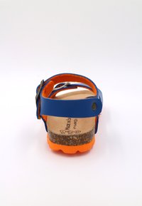 Sandale en cuir bleu avec accents orange, semelle en liège, bouclerie réglable et semelle en caoutchouc texturé. La vue arrière montre les détails des sangles.
