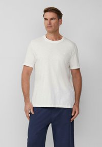 Witte t-shirt met korte mouwen van een gestructureerde stof, ronde halslijn, voorzien van een klein logo op de linkerborst, gecombineerd met marineblauwe pantalons.