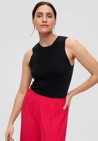 Zwarte mouwloze top met een ronde halslijn, gecombineerd met hooggeplaatste, geplooide felroze broeken met een gegatherde tailleband.