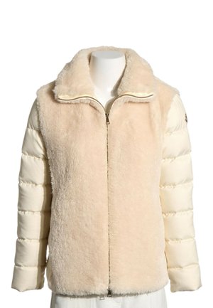 Veste beige avec un devant et un col duveteux, des manches matelassées crème et une fermeture éclair sur le devant.