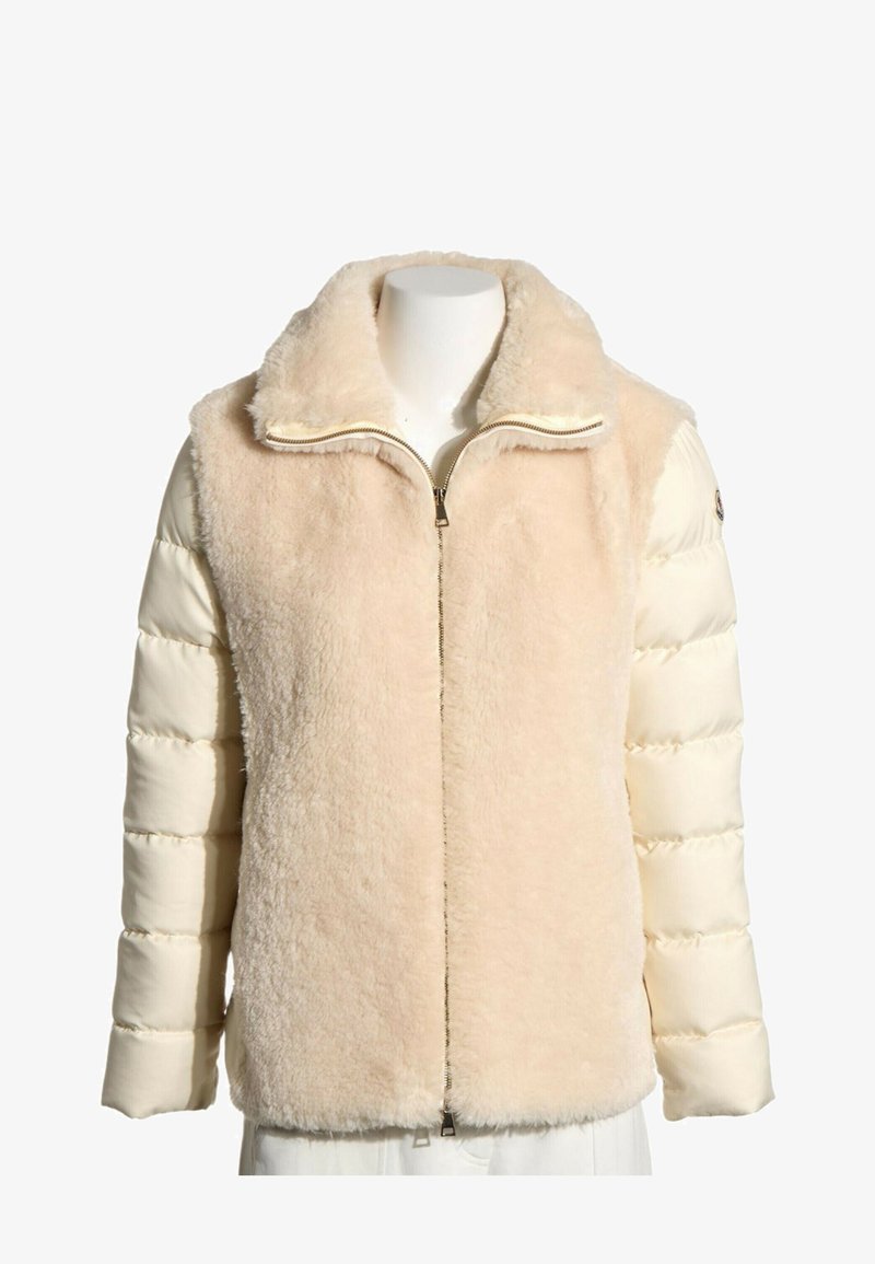 Veste beige avec un devant et un col duveteux, des manches matelassées crème et une fermeture éclair sur le devant.