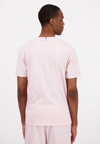 T-shirt in cotone rosa chiaro con maniche corte, colletto a giro e un piccolo dettaglio della bandiera francese sulla parte posteriore del colletto.