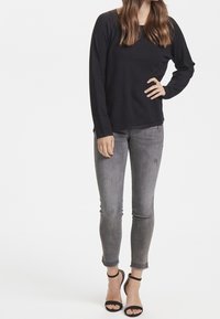 Schwarzes Langarm-Oberteil mit entspannter Passform, kombiniert mit schmal geschnittenen grauen Jeans und schwarzen High Heels mit Knöchelriemen. Einfaches Design und neutrale Farben.