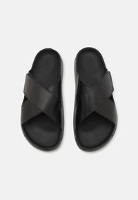 Sandali neri in pelle con design a fascia incrociata, texture liscia e suola imbottita. Stile minimalista con logo del brand impresso sulla soletta.