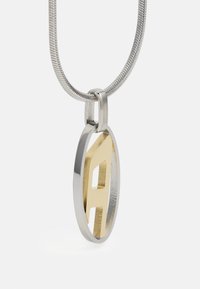 Collier en argent avec un pendentif ovale comportant une découpe de la lettre "A" en or. Fini métallisé lisse avec des lignes épurées et des couleurs contrastées.