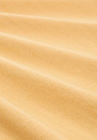 Tela de algodón en un suave tono amarillo claro, con una textura lisa y sutiles patrones de tejido diagonal, además de pliegues suaves en su caída.