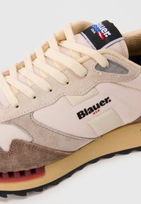 Beige and brown suede sneaker with cream laces, black and red "Blauer USA" logo, and rugged tan sole with black tread.