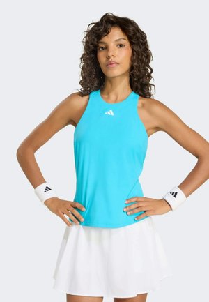 Top sportivo azzurro chiaro senza maniche con scollo arrotondato e logo Adidas. Abbinato a una gonna bianca plissettata e polsini.