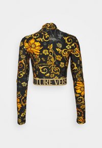 Klädd svart jacka med gyllene blommönster och text. Har långa ärmar och en glittrig gyllene nederkant med "FUTUREVERS" skrivet.