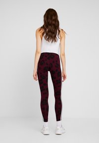 Legginsy w ciemnej bordowej barwie z czarnym wzorem kwiatowym, z białymi paskami po bokach. Wykonane z elastycznego materiału o gładkiej fakturze.