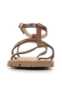 Sandali in pelle marrone con cinture sottili e fibbia. Suola in gomma con un motivo testurizzato, design aperto sulla punta e tacco piatto.