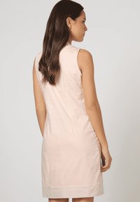 Vestido sin mangas de color rosa claro con silueta ajustada, tela suave, detalles en la costura trasera y un sutil acento en el dobladillo.