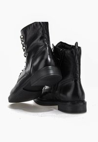 Paire de bottines en cuir noir avec fermeture éclair latérale et petit talon bloc sur fond blanc.
