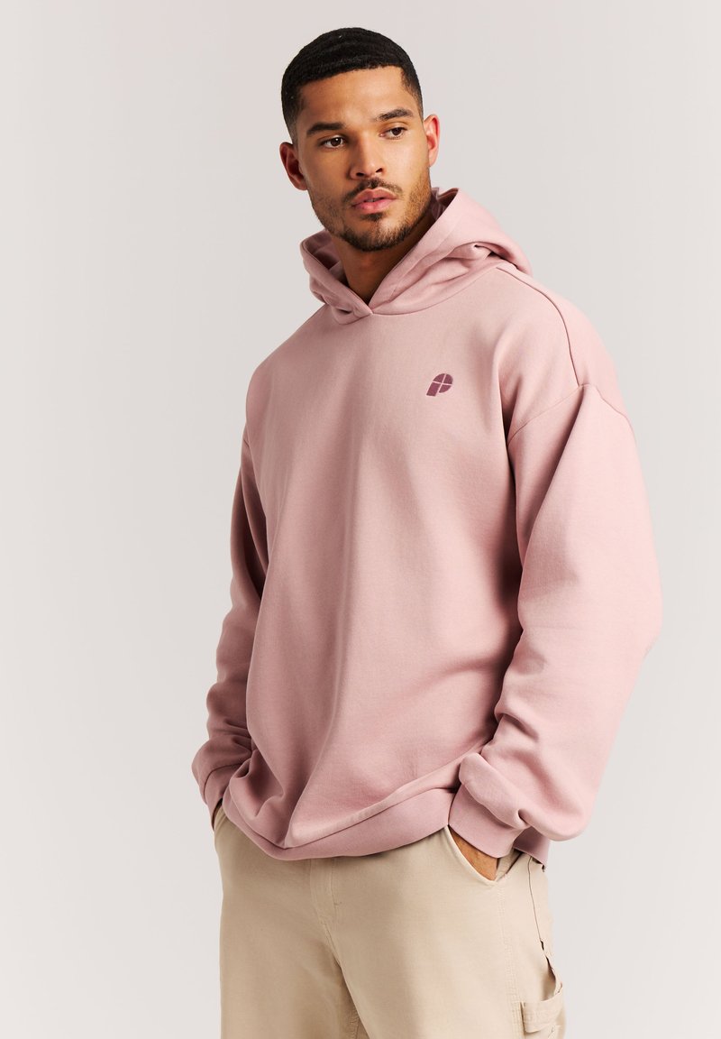 Lichtroze hoodie met een kangoeroezak en een klein logo op de borst. Heeft een ontspannen pasvorm en een verstelbare koordkap.