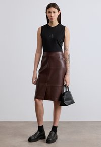 Μαύρο αμάνικο τοπ με λογότυπο, καφέ δερμάτινη μίντι φούστα, μαύρα πλατφόρμα παπούτσια και μικρή μαύρη τσάντα χειρός. Ομαλή υφή, εφαρμοστό σχέδιο.