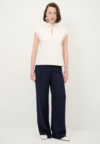 Weißes ärmelloses Oberteil mit Kragen und Schlüsselloch-Ausschnitt, kombiniert mit marineblauen weitem Hosen, die einen klaren, modernen Look kreieren.
