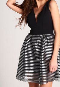 Svart bodice-klänning med djup V-ringning; silverfärgad paljettkjol med horisontella ränder; figursydd midja; texturerat material; ärmlös design.