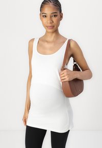Witte tanktop met een ronde hals, gecombineerd met zwarte leggings. Houdt een bruine leren handtas vast met een gebogen ontwerp.