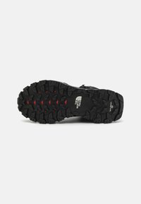 Black rubber hiking shoe outsole featuring a rugged tread pattern with deep lugs and red accents, designed for traction on various terrains.
