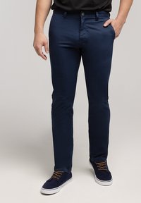 Granatowe, dopasowane bawełniane spodnie z przednimi kieszeniami i zapięciem na guziki. Noszone z ciemnymi sneakersami z brązowymi sznurowadłami.