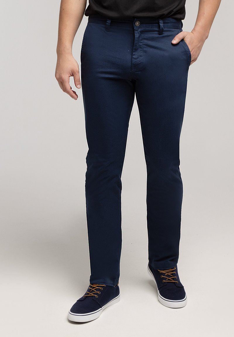 Granatowe, dopasowane bawełniane spodnie z przednimi kieszeniami i zapięciem na guziki. Noszone z ciemnymi sneakersami z brązowymi sznurowadłami.