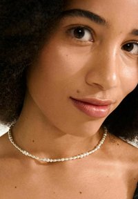 Weißes Perlenhalsband mit ovalen und runden Perlen in unterschiedlichen Größen, einem glatten Textur und einem zarten Verschluss.