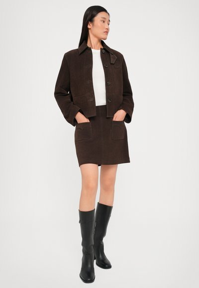 Brown suede cropped jacket with button closure, paired with a matching brown skirt featuring pockets. Model wears black knee-high boots.