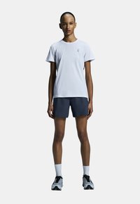 Vit kortärmad t-shirt och marinblå shorts, kombinerat med vita och svarta träningsskor. Enkel design, lätt material och minimal branding.