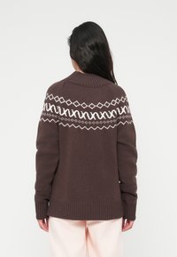 Καφέ πλεκτό πουλόβερ με λευκό γεωμετρικό μοτίβο στο στήθος, ριμπ μανσέτες και κάτω όψη, με κλασικό στρογγυλό λαιμόκοψη και μακριά μανίκια.