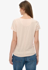Kortærmet, lyse ferskenfarvet T-shirt med rundet halsudskæring og en central syning på ryggen, kombineret med blå denimjeans.