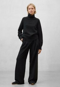 Schwarzer Rollkragenpullover mit geripptem Saum, kombiniert mit weiten schwarzen Hosen, beide in glatter Textur. Das Outfit hat eine lockere Passform.
